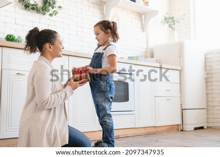 Small cute child kid daughter giving present gift box to her mom on Mother`s day Christmas New Year birthday at home kitchen. Family celebration. Happy Mother`s day!