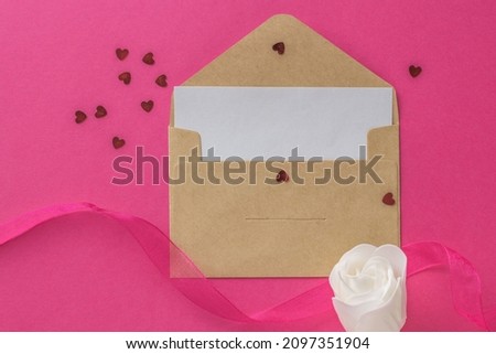 A white rosebud, an open postal envelope and a ribbon on a pink background. The concept of Valentine's Day. Flat lay.