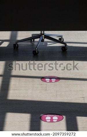 Close up light and shadow shot of red cross sticker marker warning symbol on waiting chair in office to keep space social distancing and footstep caution decal sign on floor in blurred background.