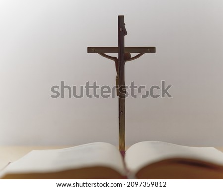 Selective focus picture of the metal cross on a white background with the blurry  book in the foreground