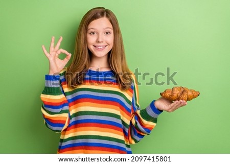 Portrait of attractive funny girly cheerful girl holding croissant showing ok-sign rate isolated over bright green color background