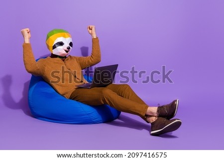 Full body portrait of crazy delighted sloth head person sit blue bag raise fists isolated on violet color background