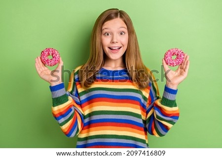 Portrait of attractive girly cheerful girl holding in hands two pink donuts isolated over bright green color background