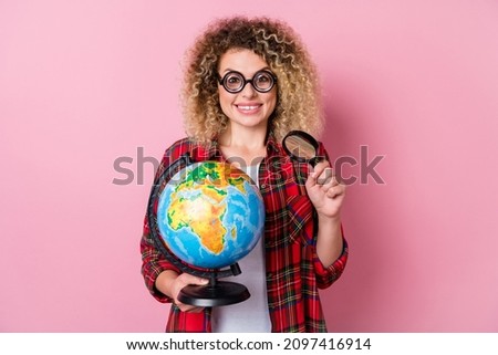 Photo of positive cheerful cute geek lady hold loupe enlarge globe wear glasses plaid shirt isolated pink color background