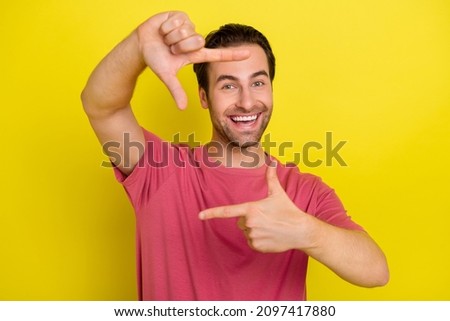 Photo of funny cheerful guy make frame gesture prepare shoot picture wear pink t-shirt isolated yellow color background