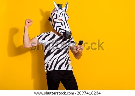 Photo of excited freak guy blogger in zebra mask use smart phone fist up win followers post isolated over yellow color background