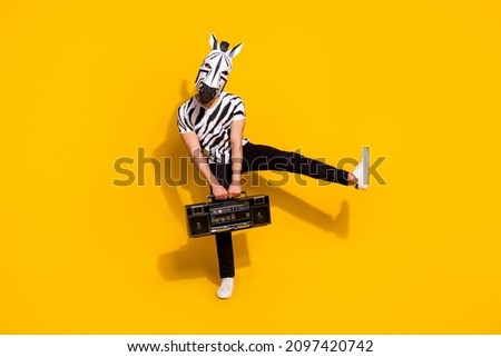 Photo of cheerful funny man wear zebra print t-shirt mask listening boombox dancing isolated yellow color background
