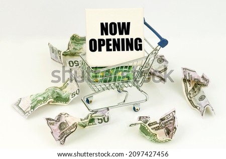 Business and economy concept. Crumpled dollars lie on a white surface, there is a cart inside a sign with the inscription - NOW OPENING