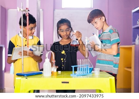 Focus on girl, Kids noting down chemicals from falsk by checking at chemistery laboratory - concept of learning reagent reaction, education and knowledge of modern science at school Royalty-Free Stock Photo #2097433975