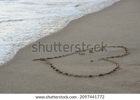 Heart drawing near the ocean waves on a beach in Thailand at sunset.