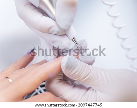 close-up photo of nail treatment with an electric file. The manicurist removes gel polish from the nail with a nail drill.