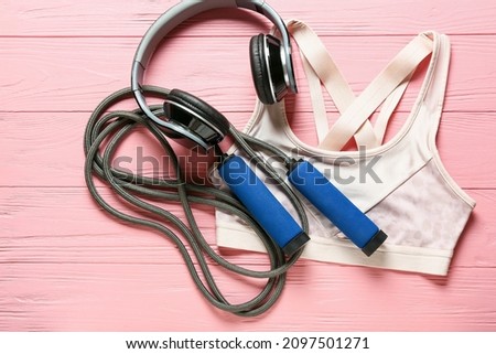 Sports top, skipping rope and headphones on color wooden background