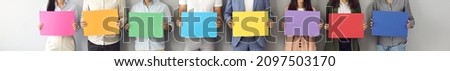 Header background with group of anonymous people standing by white grey studio wall and holding colorful blue, red, green, yellow, purple, orange and pink empty sheets of paper as mockup sign banners