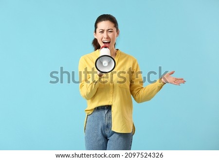 Angry young woman with megaphone on color background Royalty-Free Stock Photo #2097524326