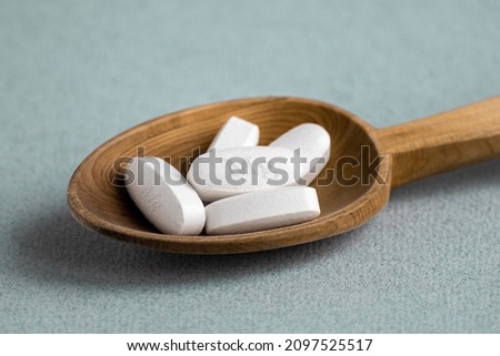 Tablets , vitamins with the abbreviation Mg ( magnesia, the macronutrient magnesium ) lying in a wooden spoon on a light background. Copy space. Royalty-Free Stock Photo #2097525517