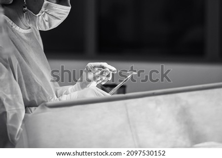 A surgeon wearing sterile gloves operates with a needle holder, a surgical needle and a surgical thread. Selective focus. Black and white photo.