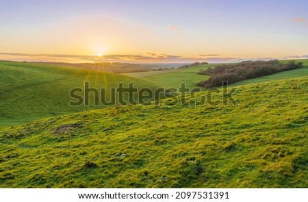 a golden sunset, low illuminated cloud on the horizon over a deep green grass valley, North Wessex Downs AONB