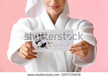 Young woman in bathrobe with gift voucher on pink background, closeup
