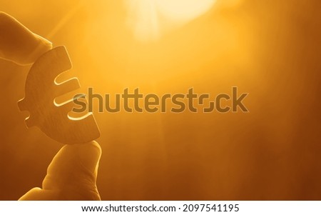 man's hand hold the Euro icon silhouette against sunny blue, yellow sky. sun rays. euro sign, symbol of money, idea of Euro Union.