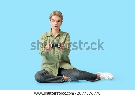 Shocked young woman with game pad on blue background