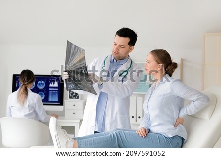 Young doctor showing x-ray image of spine to patient in clinic Royalty-Free Stock Photo #2097591052