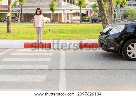 The girl crosses the street at a pedestrian crossing. The child goes to school.