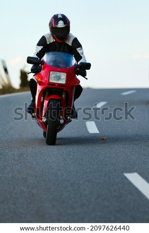 Red motorcycle with driver in leather suit while driving on a road with a slight side position, photographed from the front.
 Royalty-Free Stock Photo #2097626440