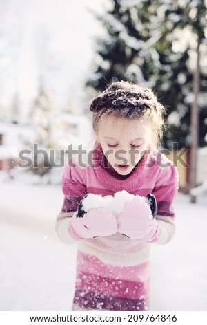 Adorable little girl in knit  pink dress playing with the snow outdoors