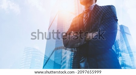 Double exposure of businessman wearing a suit and standing with arms crossed with city building background. 