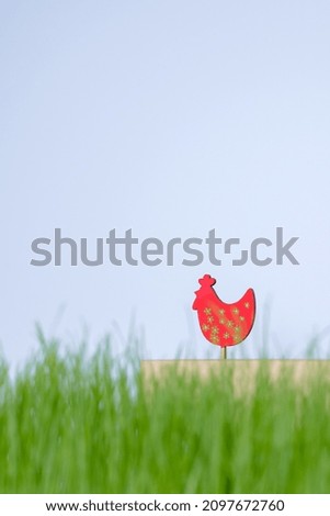Decorative red chicken over green grass on a blue background. High quality photo