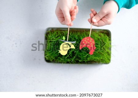 Decorative red chicken and a bird in the hands of a child over green grass on a white background. High quality photo