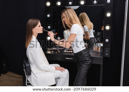 side view of blonde makeup artist applying face powder on professional model