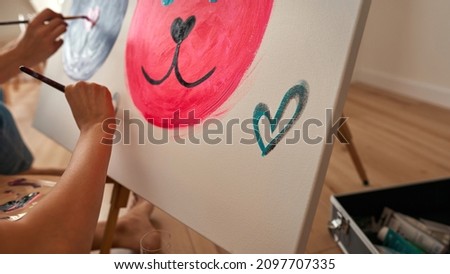Cropped image of girls painting picture of mouse heads with paints on easel at home. Concept of domestic entertainment, hobby and leisure. Girlfriends spending time together. Daytime