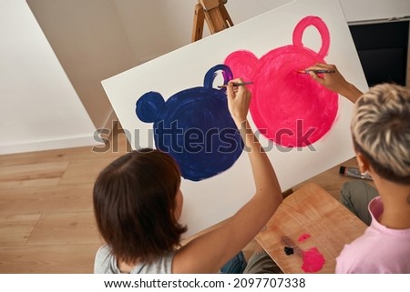 Partial image of young lesbian girls painting picture of mouse heads with pink and purple paints at home. Domestic entertainment, hobby and leisure. Homosexual relationship and spending time together