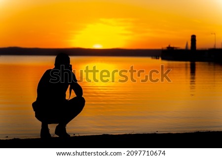 A silhouette of a photographer taking pictures of the sea at sunset