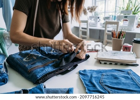 Sustainable fashion, Denim Upcycling Ideas, Using Old Jeans, Repurposing Jeans, Reusing Old Jeans, Upcycle Stuff. Woman seamstress cut and repair old blue jeans in sewing studio. Royalty-Free Stock Photo #2097716245