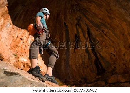 A man is engaged in rock climbing, stands against the background of a beautiful red cave before training, the climber leads an active lifestyle and is involved in extreme sports in Greece, Twin Caves.