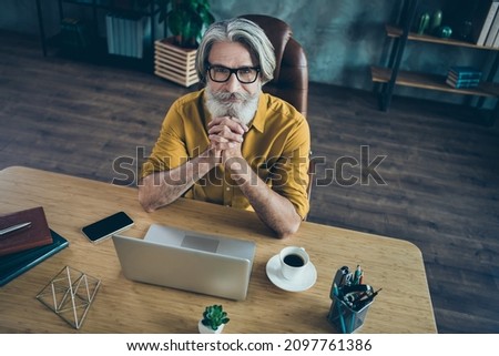Photo of thoughtful senior man wear yellow shirt glasses arms chin working modern device indoors workshop workstation