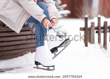 A girl laces up her skates while sitting on a park bench. A young woman came to skate at the rink.