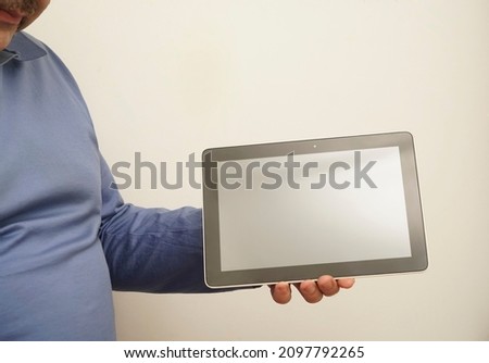 man isolated on gray background standing in blue  shirt holding tablet and showing it blank screen  as if advising product or service. Studio picture  