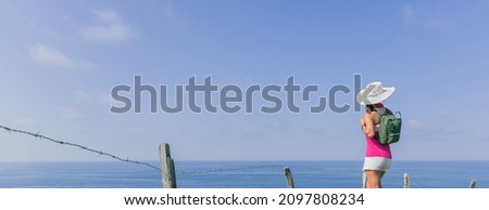 a woman with a green backpack and white hat in front of the sea and blue sky.concept tourism and outdoor freedom.