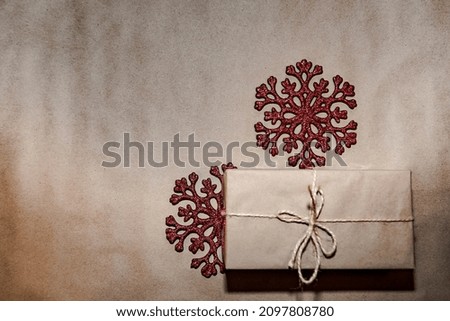a close-up gift in craft paper lies on a background with two red snowflakes