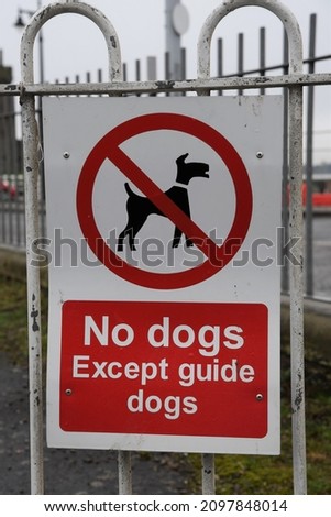 No dogs except guide dogs sign in the UK. Red and white sign on white railings.