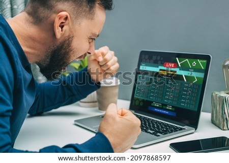 Male fan watching football play online broadcast on his laptop, cheering for favourite team and betting at bookmaker's website. Lucky man celebrating victory after winning jackpot in online casino. Royalty-Free Stock Photo #2097868597