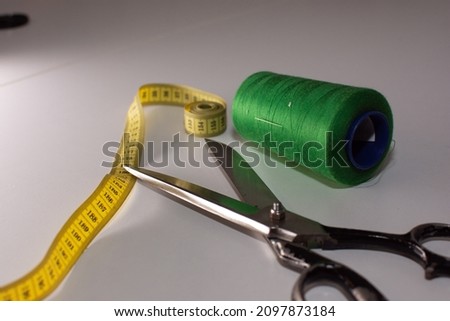 Professional sewing supplies on white desk. Scissors, thread, and meter for body measurements on white background.