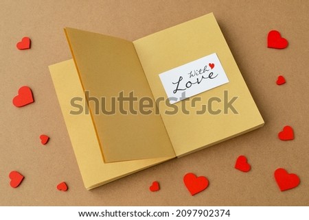 red valentine hearts a blank paper notebook and a card "With love" on a background of kraft paper