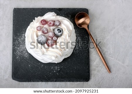Sweet white meringue dessert on black stone plate with bronze spoon