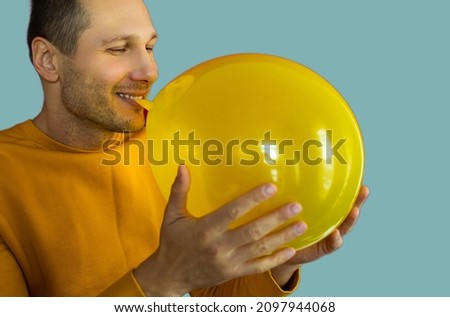 portrait of young man blowing a yellow balloon over blue background.