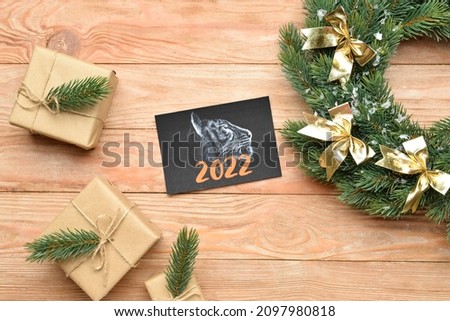 Greeting card for New Year 2022 celebration with gifts and wreath on wooden background