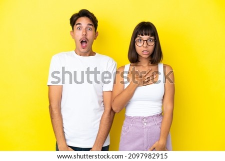 Young mixed race couple isolated on yellow background with surprise and shocked facial expression